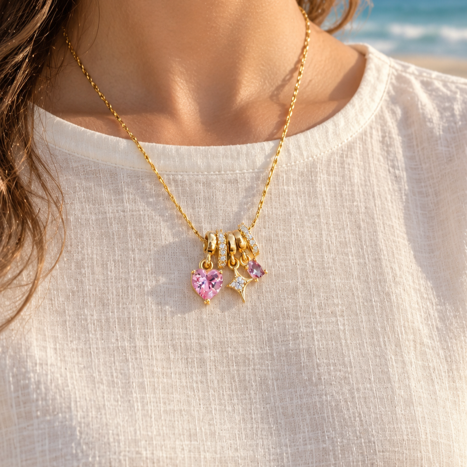 Gold-tone necklace with multiple pink heart and star charm pendants worn on a beach