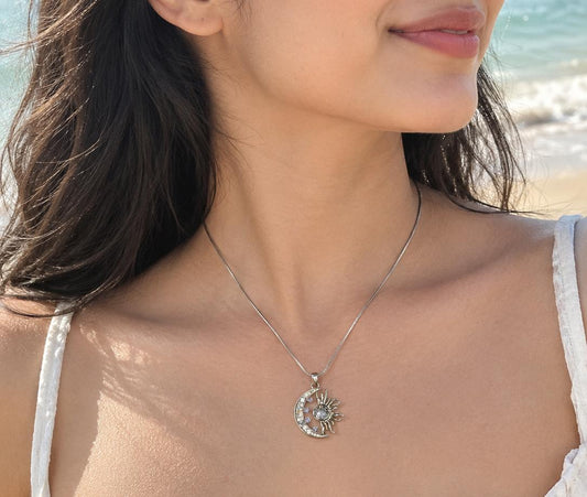 Silver-tone crescent moon and sun pendant necklace worn on a beach