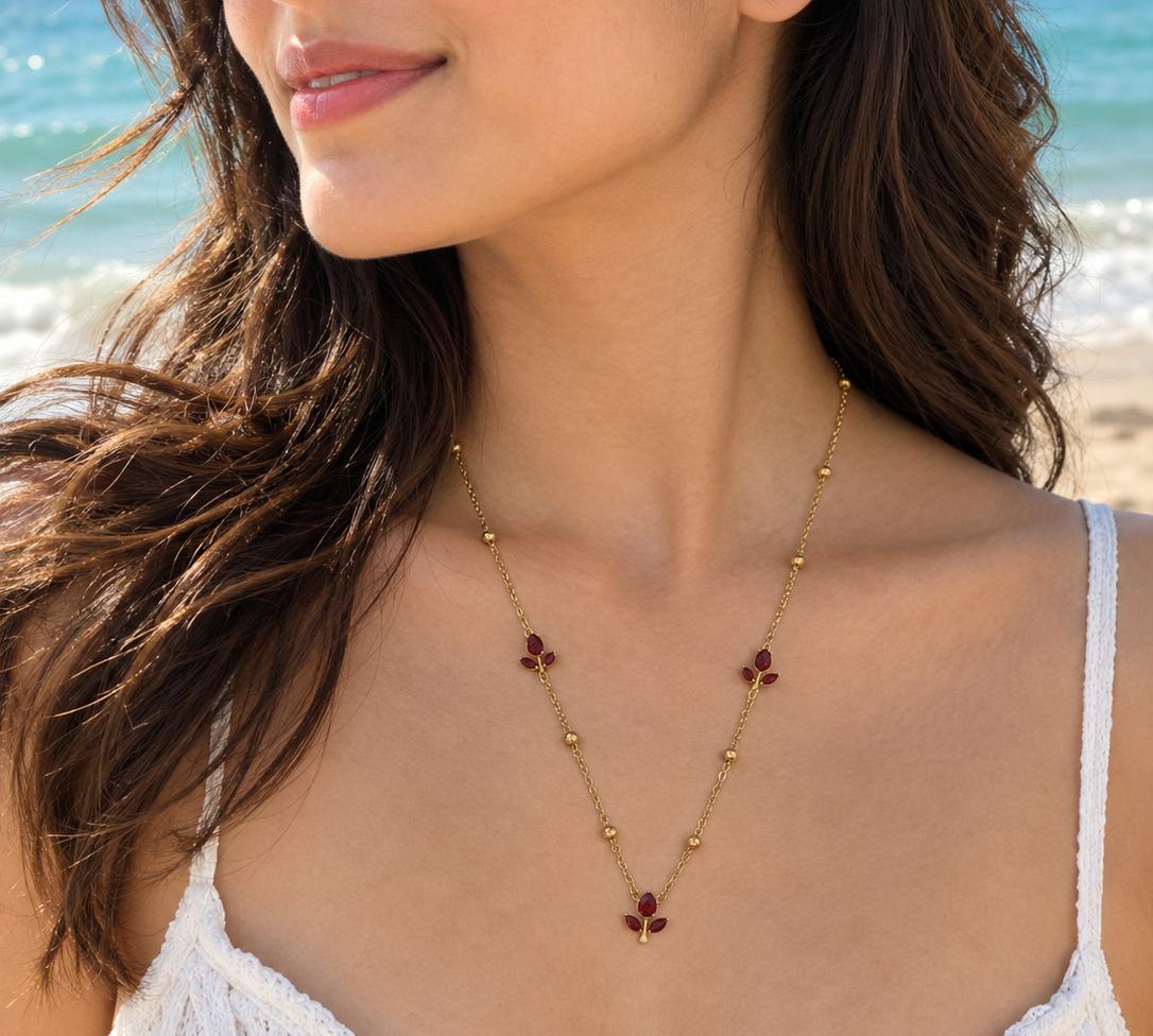 Gold-tone necklace with red floral gemstone accents worn on a beach