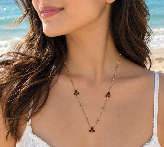 Gold-tone necklace with red floral gemstone accents worn on a beach