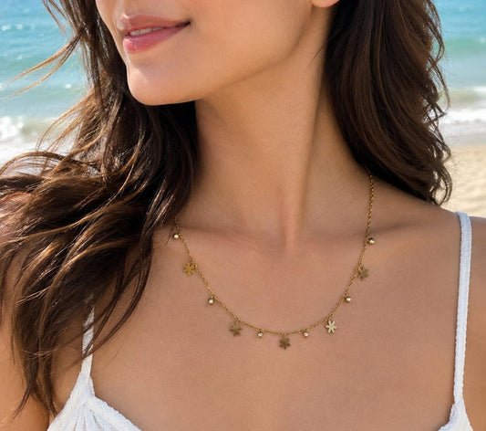 Gold-tone necklace with petite floral and green crystal pendant worn on a beach