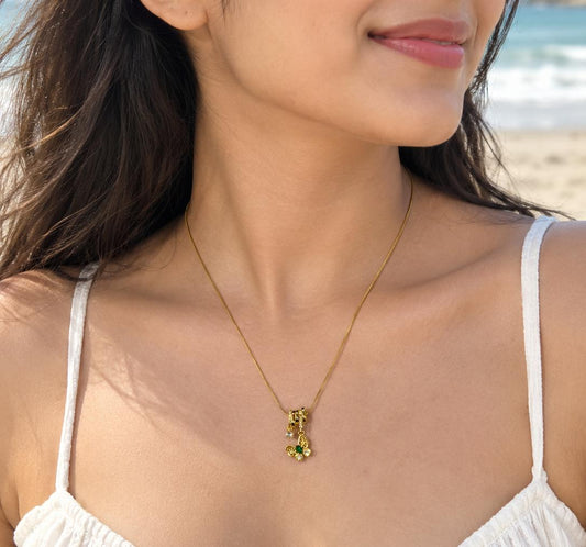 Gold-tone necklace with floral green and clear crystal pendant worn on a beach
